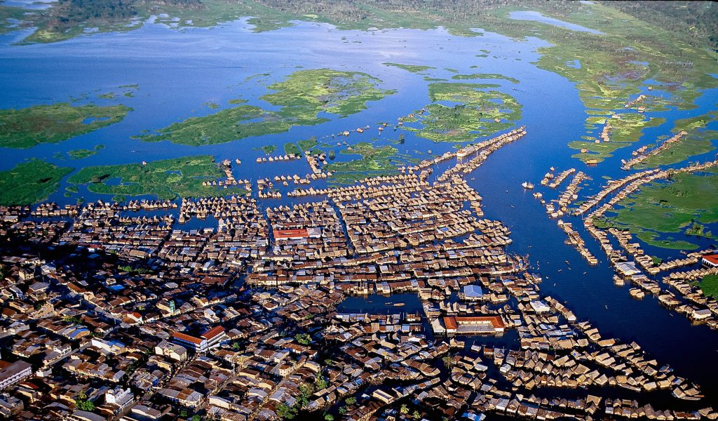 Luftaufnahme der peruanischen Amazonasstadt Iquitos in der Region Loreto. Dicht bebaute Stadtviertel gehen in ein weit verzweigtes Netz aus Wasserstraßen über, entlang derer zahlreiche Häuser auf Stelzen oder schwimmende Gebäude liegen. Große Wasserflächen mit Inseln aus dichter Vegetation umgeben die Stadt und verdeutlichen ihre Lage im Überschwemmungsgebiet des Amazonas.