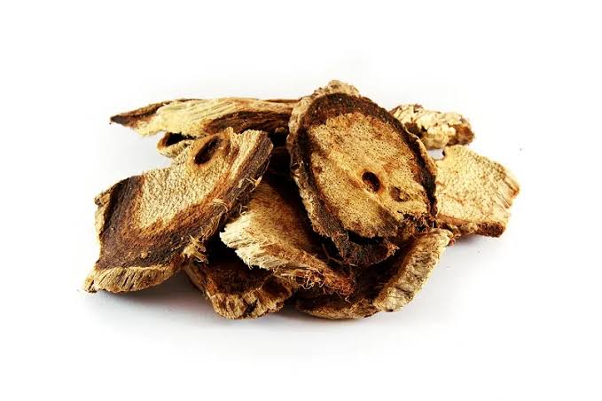Getrocknete Wurzelscheiben von Butea superba auf weißem Hintergrund. Die unregelmäßig geschnittenen, rundlichen bis ovalen Scheiben zeigen eine hellbeige bis gelblich-braune Schnittfläche mit dunkler brauner Rinde. Die getrocknete Wurzel wird in der traditionellen Pflanzenheilkunde verwendet.