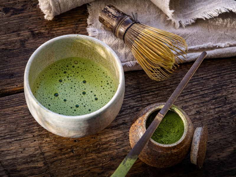 Zubereiteter Matcha in einer Keramikschale mit Bambusbesen (Chasen), Matcha-Pulver und Bambuslöffel (Chashaku).