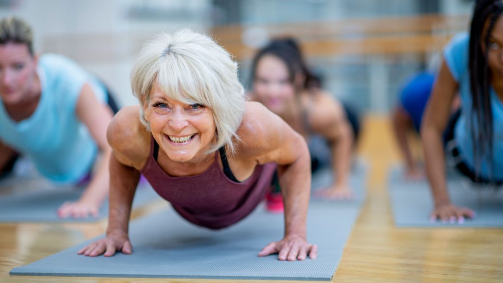 Lächelnde Frau macht gemeinsam mit weiteren Frauen Liegestütze auf einer Trainingsmatte.