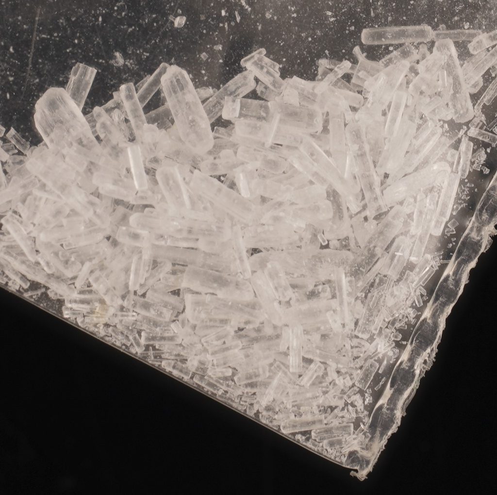Makroaufnahme farbloser, transparenter Kristalle mit länglicher, prismatischer Form in einem transparenten Plastikbeutel. Das Material wird als Ketamin dargestellt.