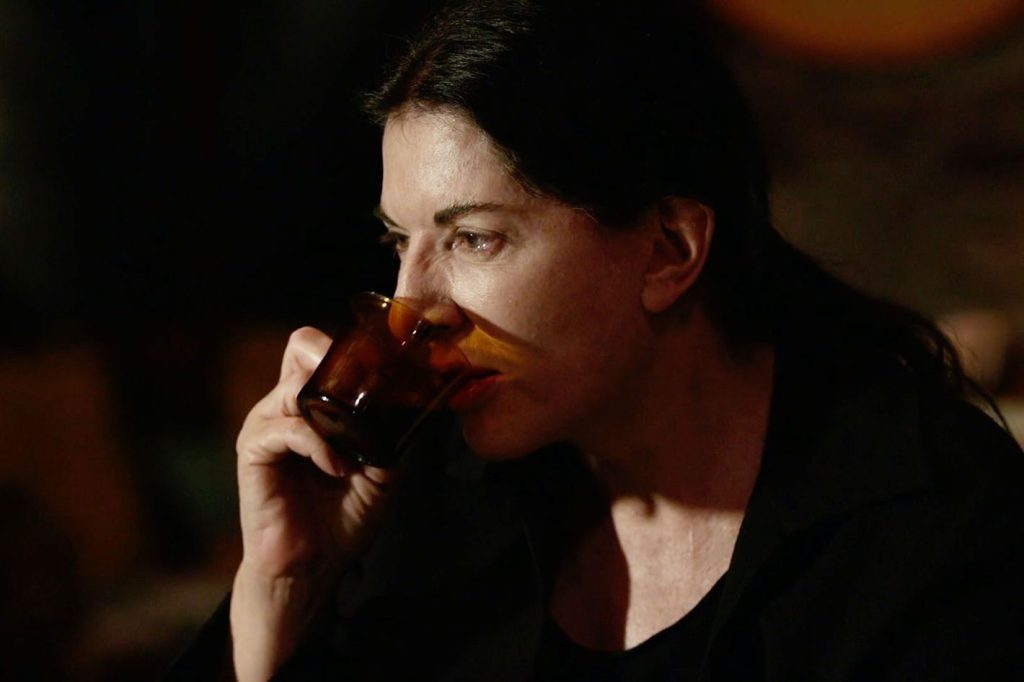 Marina Abramović hält während einer Performance ein braunes Glas an ihr Gesicht.
