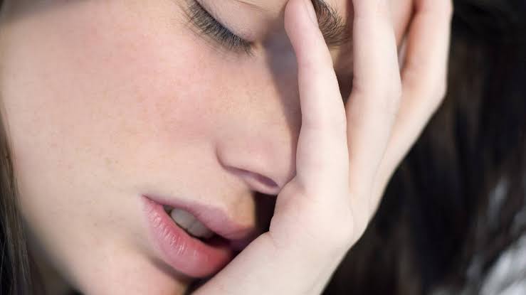 Depressionen: erschöpfte Person mit geschlossenen Augen hält sich die Hand vors Gesicht.