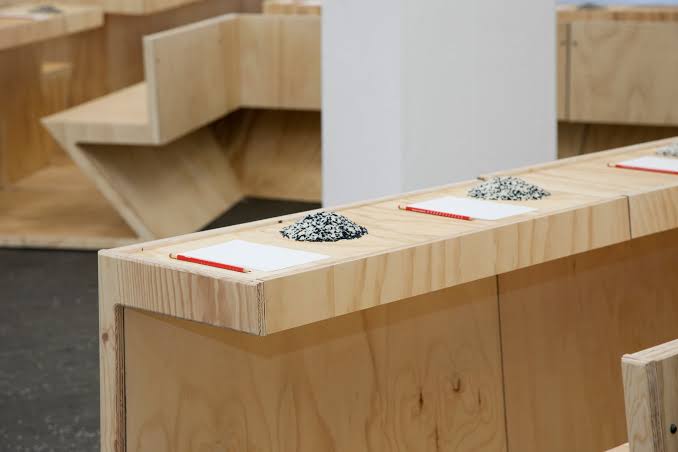    Installation des Marina Abramović Institute mit Holztischen, Papier, roten Bleistiften und kleinen Häufchen aus schwarzen und weißen Reiskörnern.