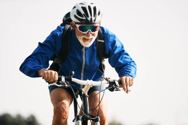 Älterer Mann mit weißem Bart, Fahrradhelm und Sonnenbrille fährt sportlich mit dem Fahrrad.