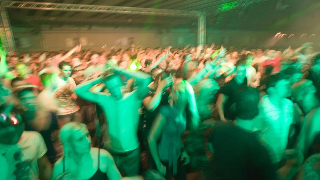 Dicht gedrängte Menschen tanzen auf einer Techno-Party unter grünem Clublicht – ausgelassene Stimmung in der Technoszene.