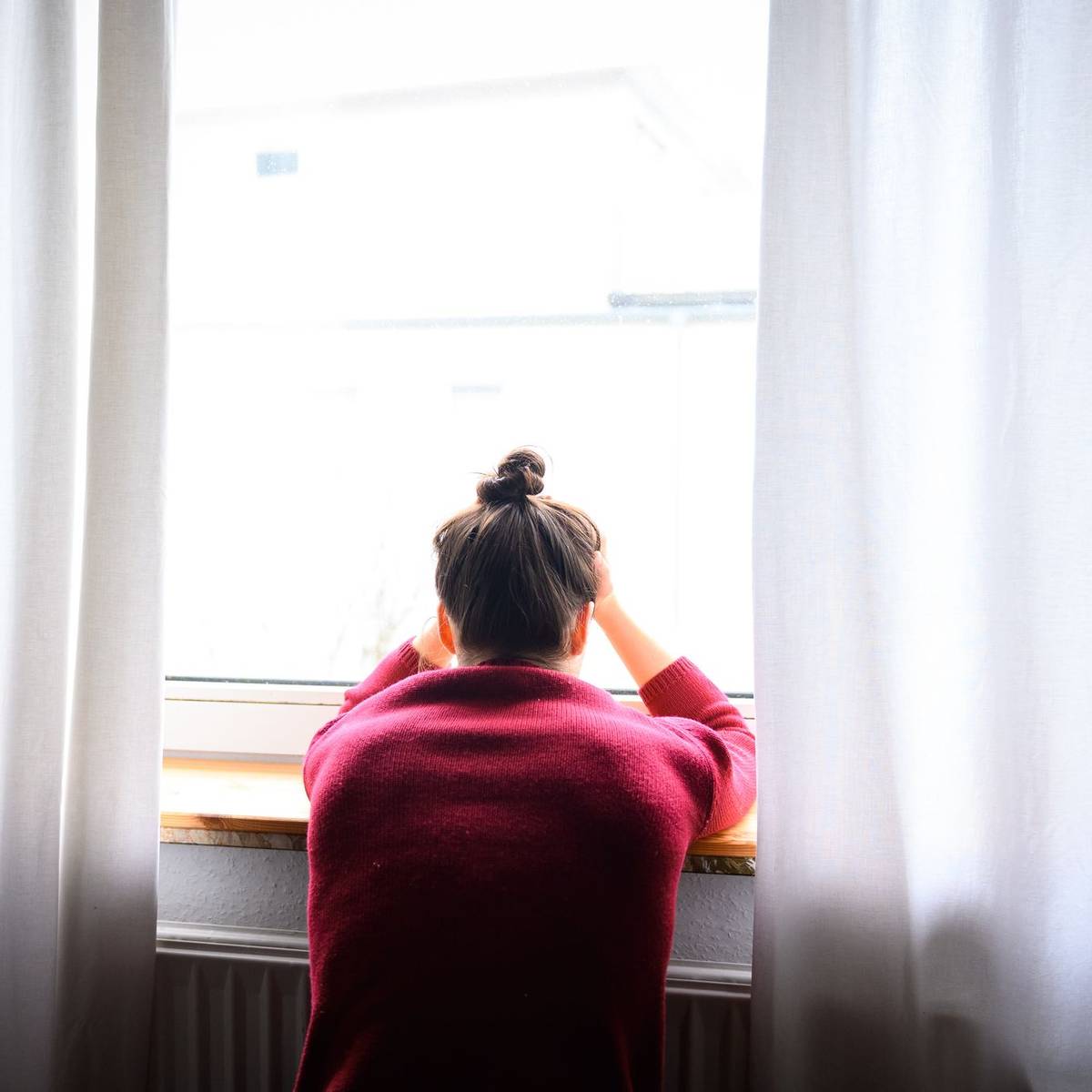 Nachdenkliche Person sitzt am Fenster als Symbol für Depression und psychische Belastung