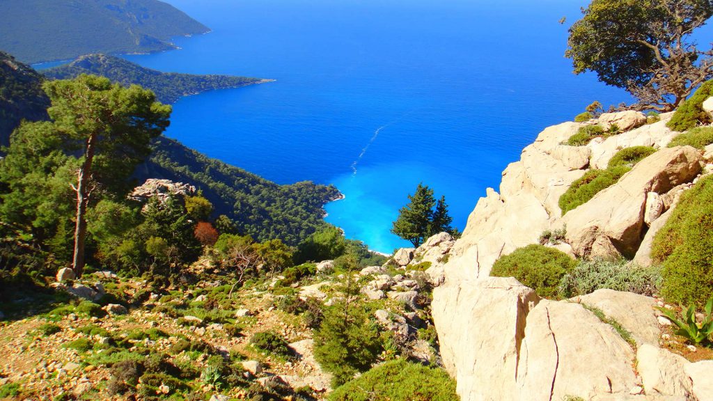 Blick vom felsigen, bewaldeten Ida-Gebirge in der Türkei auf das tiefblaue Ägäische Meer, eine türkisfarbene Bucht und mehrere grüne Landzungen.