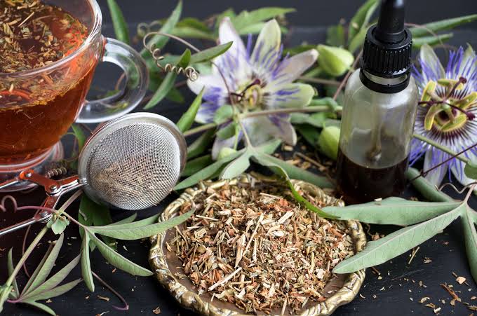 Passionsblumentee mit getrocknetem Pflanzenmaterial, Teesieb und Tropfflasche, umgeben von frischen Passionsblüten und Blättern.