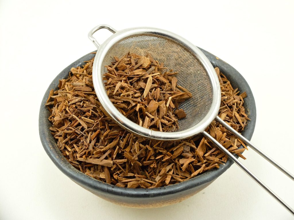 Geschnittene Yohimbe-Rinde (Pausinystalia johimbe) mit Teesieb – traditionell verwendete afrikanische Baumrinde mit dem Indolalkaloid Yohimbin